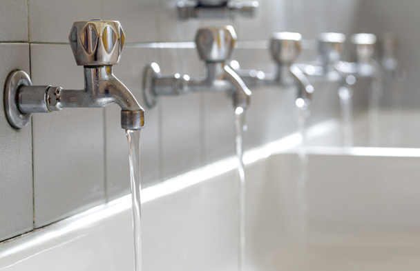 robinets en acier avec de l'eau potable coulant dans la salle de bain du collège
 - Photo, image