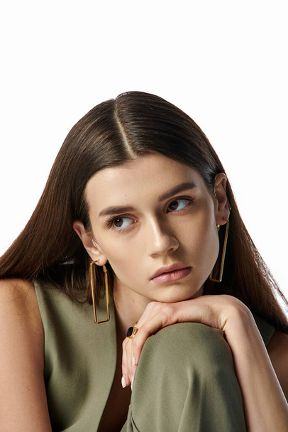 A stylish, elegant woman with beautiful long brown hair and gold earrings posing against a gray backdrop. - Photo, Image