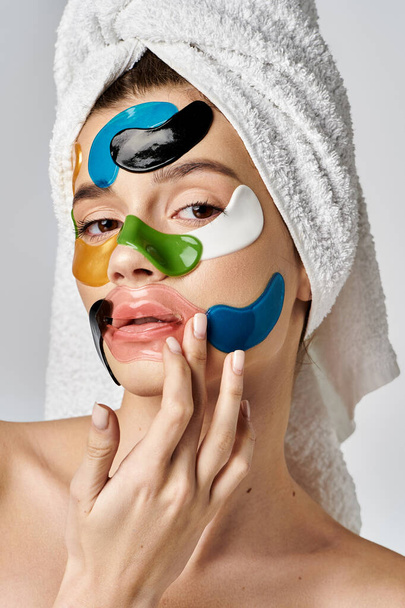 Une superbe jeune femme avec une serviette enroulée autour de sa tête avec des patchs sur son visage, mettant en valeur sa beauté naturelle. - Photo, image