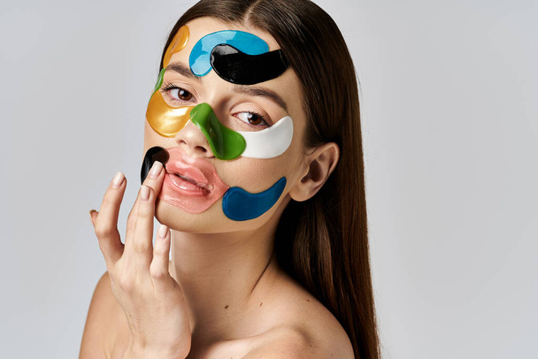 Een jonge vrouw met ooglapjes op haar gezicht, presentatie van een kleurrijke en creatieve make-up look met gedurfde kleuren en overdreven functies. - Foto, afbeelding