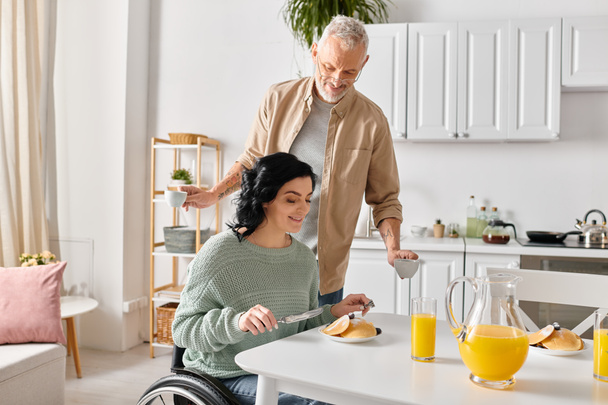 Una mujer discapacitada en silla de ruedas y su marido cocinando juntos en su cocina en casa. - Foto, Imagen