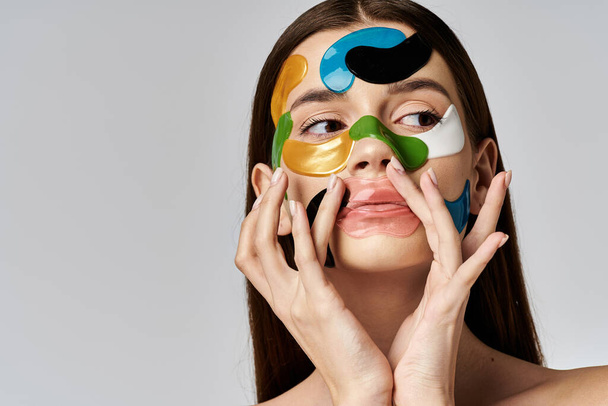A young woman with eye patches on her face and hands delicately holds them up to her face in a serene pose. - Photo, Image