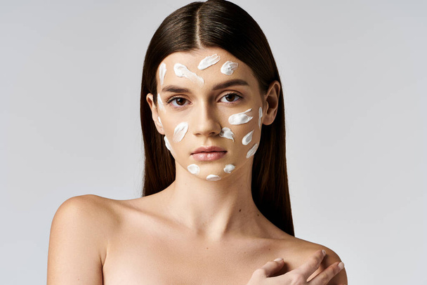Молода жінка з яскравим білим кремом на обличчі витончено позує, обіймаючи свою унікальну красу. - Фото, зображення