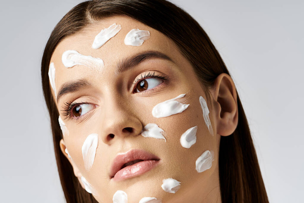 Красивая молодая женщина с кучей крема на лице, демонстрирующая свои привычки по уходу за кожей. - Фото, изображение