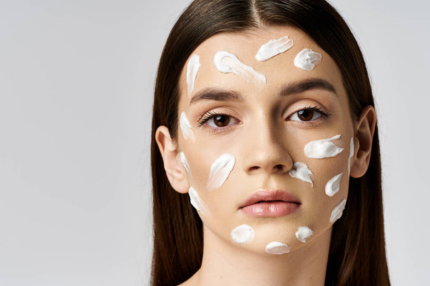 A beautiful young woman poses wearing a white cream on her face, exuding elegance and mystery. - Photo, Image
