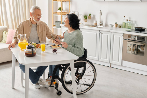 Tekerlekli sandalyede bir adam ve bir kadın evlerindeki mutfaklarında birlikte oturuyorlar.. - Fotoğraf, Görsel