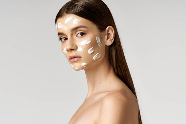 Una giovane donna in posa con uno spesso strato di crema sul viso, creando un'immagine stravagante e surreale. - Foto, immagini