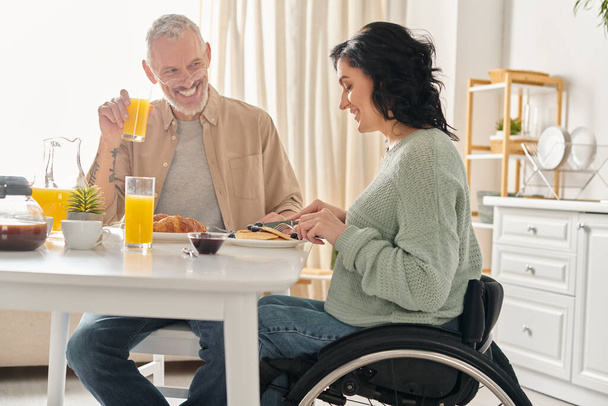 車椅子の男女が自宅のキッチンで一緒に朝食を楽しんでいる. - 写真・画像