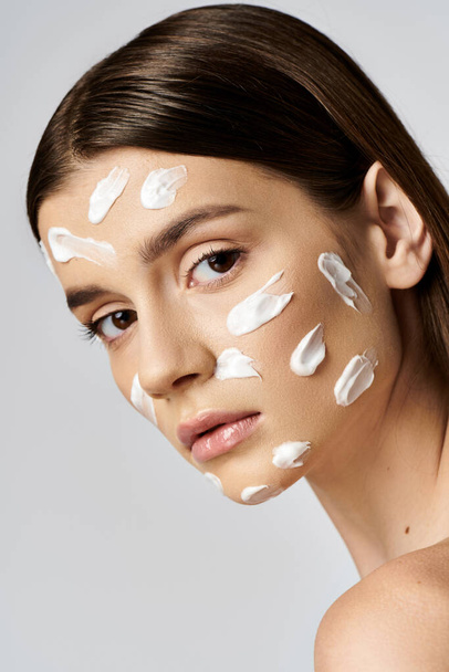 A beautiful young woman with white cream on her face poses in a serene and artistic manner. - Photo, Image