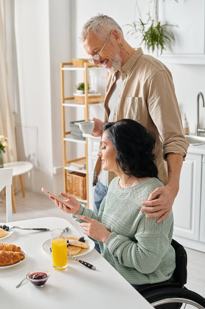 Un couple marié, le mari et la femme handicapée, partagent un repas ensemble à une table de cuisine dans leur maison. - Photo, image