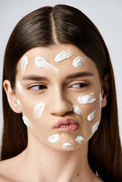 Una hermosa joven con una gruesa capa de crema blanca en la cara, creando un aspecto llamativo y etéreo. - Foto, Imagen