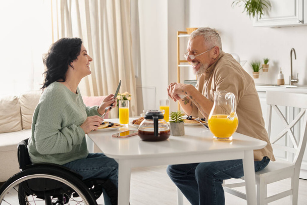 Un uomo e una donna in sedia a rotelle impegnati in una conversazione in un ambiente cucina domestica. - Foto, immagini