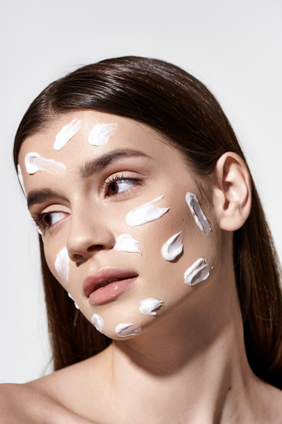 A beautiful young woman poses gracefully with a white cream on her face, exuding an air of mystery and elegance. - Photo, Image