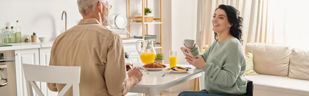 Zdravotně postižená žena na invalidním vozíku a její manžel sedí společně u kuchyňského stolu a sdílejí klidný okamžik.. - Fotografie, Obrázek