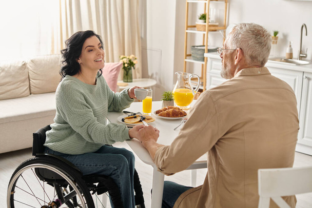 Niepełnosprawna kobieta na wózku inwalidzkim jest z miłością podawana przez męża soku pomarańczowego w ich kuchni.. - Zdjęcie, obraz