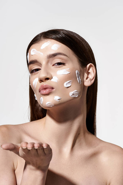 Une belle jeune femme portant une crème blanche sur son visage, ajoutant un élément de mystique et d'élégance à son apparence. - Photo, image