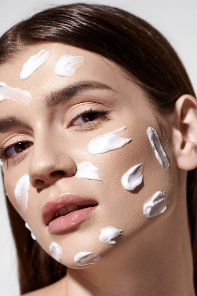 Een mooie jonge vrouw die vol vertrouwen huidverzorging omarmt met een royale hoeveelheid crème op haar gezicht. - Foto, afbeelding