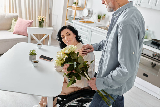 Een man staat bij zijn vrouw rolstoel in hun keuken, met onwrikbare steun en liefde. - Foto, afbeelding
