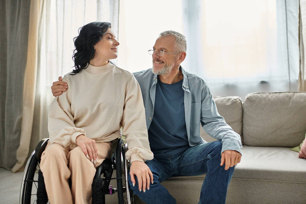 Zdravotně postižená žena na invalidním vozíku si povídá s mužem v obývacím pokoji. - Fotografie, Obrázek