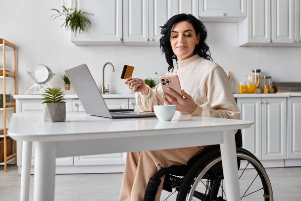 Donna su una sedia a rotelle che gestisce le finanze e lavora online utilizzando un computer portatile nella sua cucina. - Foto, immagini