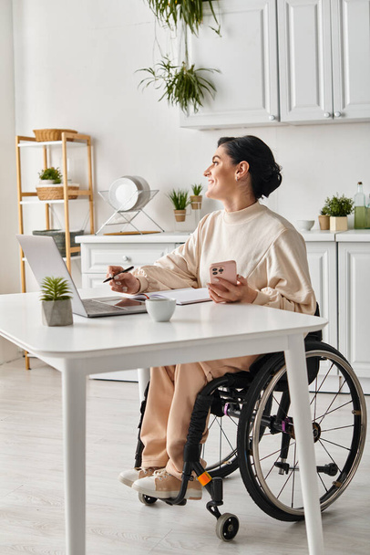 une femme handicapée dans un fauteuil roulant travaillant sur un ordinateur portable dans sa cuisine - Photo, image