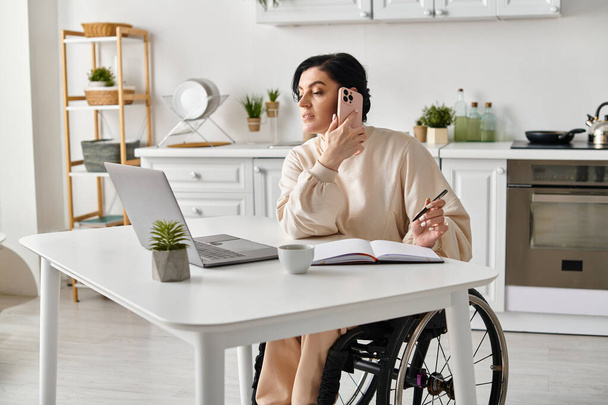 Femme en fauteuil roulant travaillant à distance, bavardant sur un téléphone portable dans la cuisine. - Photo, image