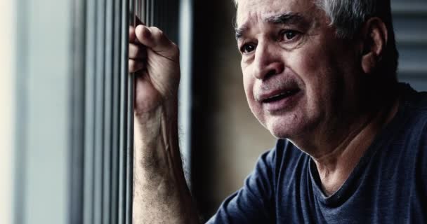 Zdesperowany starszy mężczyzna płaczący w smutku i depresji przedstawiający chorobę w podeszłym wieku. lat 70-tych płaczliwy starszy mężczyzna zbliżenie twarz chwytając na metalowy bar uczucie uwięziony i wstyd z przeszłości żale - Materiał filmowy, wideo