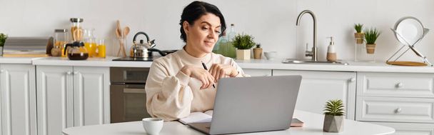 nő ül a konyhaasztalnál, összpontosít a laptop képernyőjén, miközben távolról dolgozik. - Fotó, kép