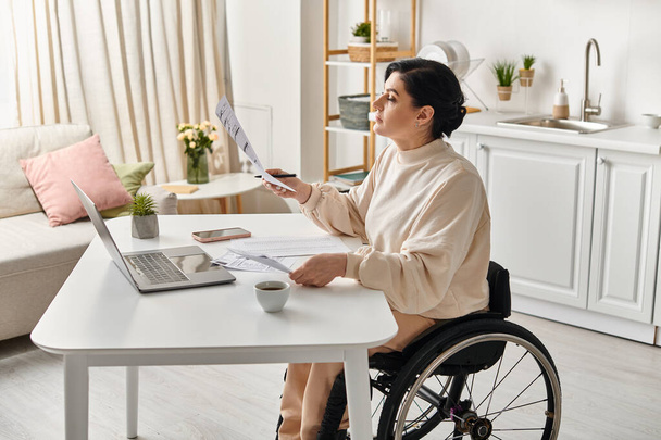 Une femme handicapée dans un fauteuil roulant travaillant sur un ordinateur portable dans sa cuisine, montrant l'autonomisation et le progrès technologique. - Photo, image