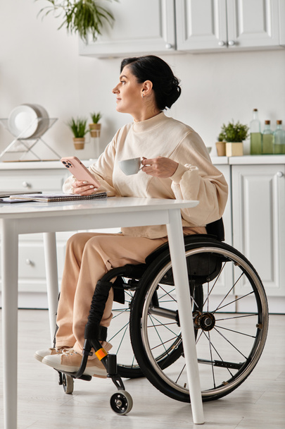 Kobieta na wózku inwalidzkim pracująca na laptopie przy stole w kuchni, wykazująca determinację i skupienie. - Zdjęcie, obraz
