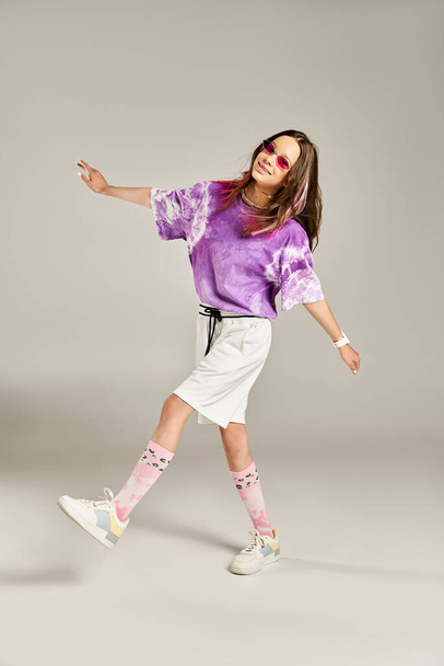 Una vibrante adolescente alcanza una pose juguetona con una elegante camisa púrpura y pantalones cortos blancos. - Foto, imagen