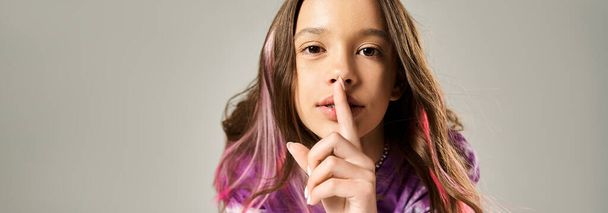 Стильная девочка-подросток с длинными волосами прижимает палец к губам скрытным жестом. - Фото, изображение