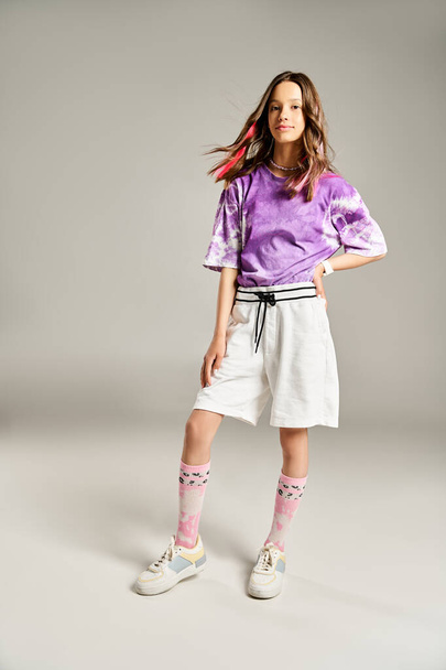 Стильная девушка-подросток в фиолетовой рубашке и белых шортах занимает активную позу, излучая яркость и изящество. - Фото, изображение