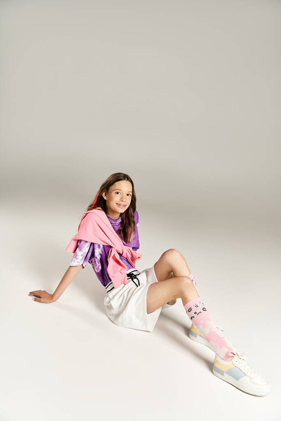Ένα κομψό, ζωντανό έφηβο κορίτσι κάθεται στο έδαφος, τα πόδια σταυρωμένα, συμμετέχοντας σε ενεργό στοχασμό. - Φωτογραφία, εικόνα