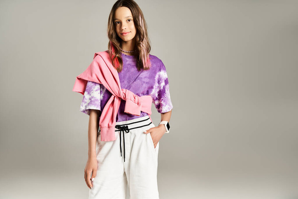 Ein gut aussehendes Teenager-Mädchen posiert dynamisch in stilvoller Kleidung, trägt ein lila Hemd und eine weiße Hose. - Foto, Bild