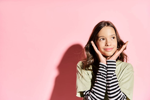 Ein stilvolles Teenager-Mädchen posiert, die Hände auf dem Gesicht, verströmt Vertrauen und Schönheit in lebendiger Kleidung. - Foto, Bild
