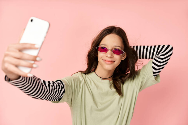 Chica adolescente con estilo en traje vibrante toma selfie con el teléfono celular, usando gafas de sol fresco. - Foto, Imagen