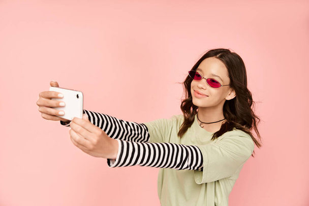 Una ragazza adolescente alla moda in abiti vibranti e occhiali da sole che si fa un selfie con un cellulare. - Foto, immagini