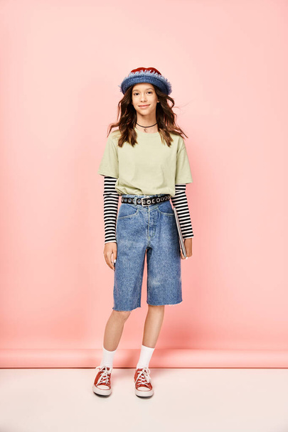 Ein stilvolles Teenager-Mädchen posiert aktiv in einem lebendigen Outfit, mit Hut und Shorts. - Foto, Bild