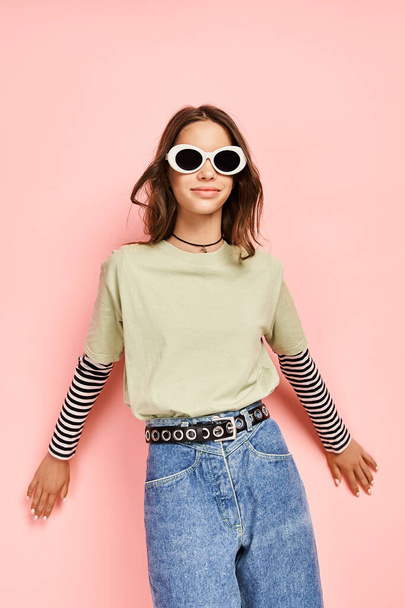 Ένα κομψό έφηβο κορίτσι σε ένα πράσινο πουκάμισο χτυπώντας μια στάση με γυαλιά ηλίου, αποπνέοντας αυτοπεποίθηση και δροσιά. - Φωτογραφία, εικόνα