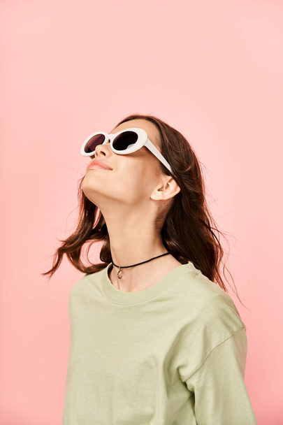 Una giovane donna alla moda in abiti vibranti, con gli occhiali da sole, alza lo sguardo pensieroso verso il cielo. - Foto, immagini
