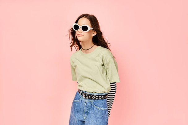 Ένα κομψό έφηβο κορίτσι με αυτοπεποίθηση θέτει σε ένα πράσινο πουκάμισο και γυαλιά ηλίου, αποπνέοντας μια ζωντανή και ενεργειακή αύρα. - Φωτογραφία, εικόνα