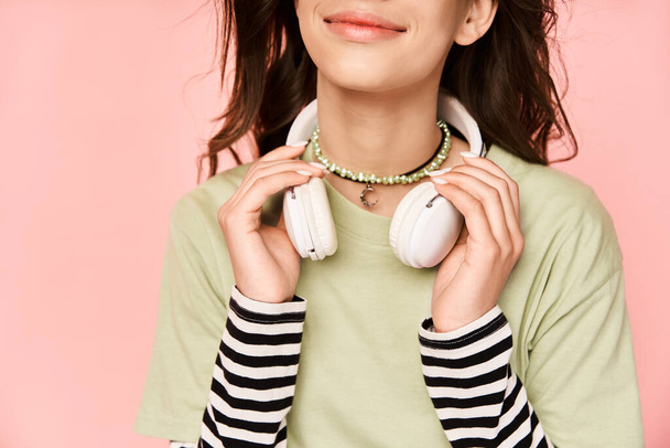Ένα ζωντανό, στιλάτο έφηβο κορίτσι που φοράει ακουστικά και πράσινο πουκάμισο, πετυχαίνοντας μια δυναμική στάση. - Φωτογραφία, εικόνα