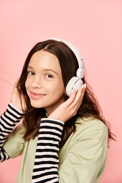 Ένα κομψό έφηβο κορίτσι χαμογελά έντονα, ενώ φοράει ακουστικά, αποπνέοντας ευτυχία και ενέργεια. - Φωτογραφία, εικόνα