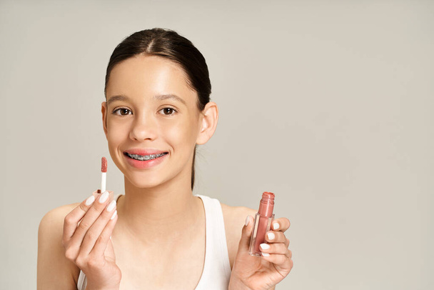 Una adolescente con estilo en traje vibrante sosteniendo dos lápices labiales en sus manos, exudando confianza y belleza. - Foto, imagen