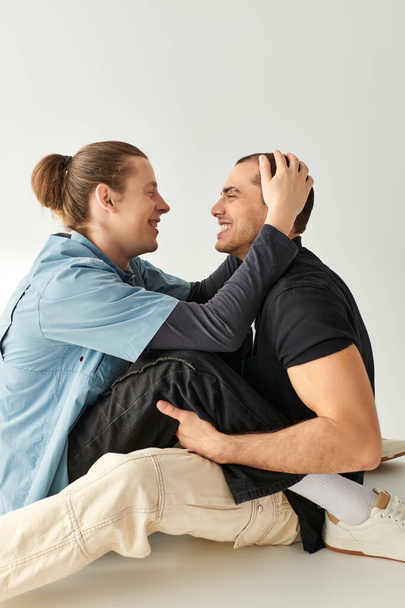 Двое мужчин сидят близко на полу, разделяя момент близости и связи. - Фото, изображение