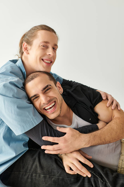 Двое мужчин проявляют привязанность, сидя на диване и обнимаясь друг с другом.. - Фото, изображение