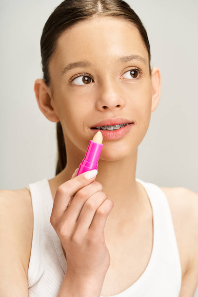 Trendy tienermeisje in trendy kleding houdt een roze lippenstift in de hand. - Foto, afbeelding