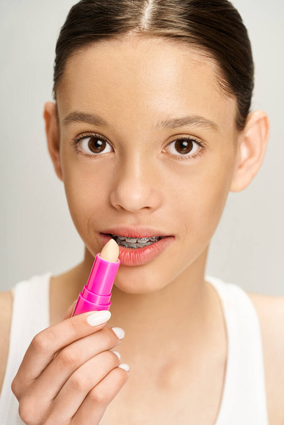 Ein stilvolles, gut aussehendes Teenie-Mädchen in lebendiger Kleidung trägt leidenschaftlich rosa Lippenstift auf ihre Lippen auf und unterstreicht ihre Schönheit. - Foto, Bild