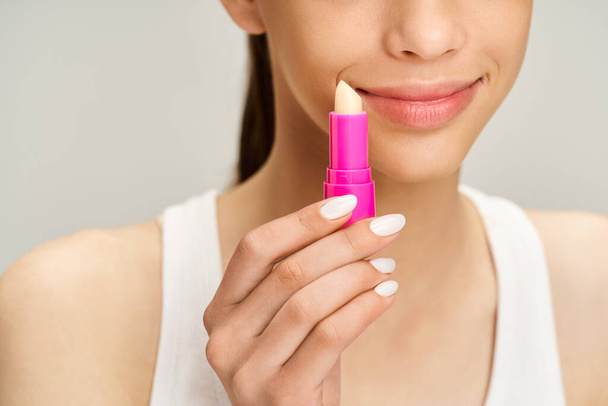 Teenage girl in stylish attire, energetically holds a lip balm, showcasing beauty and confidence. - 写真・画像